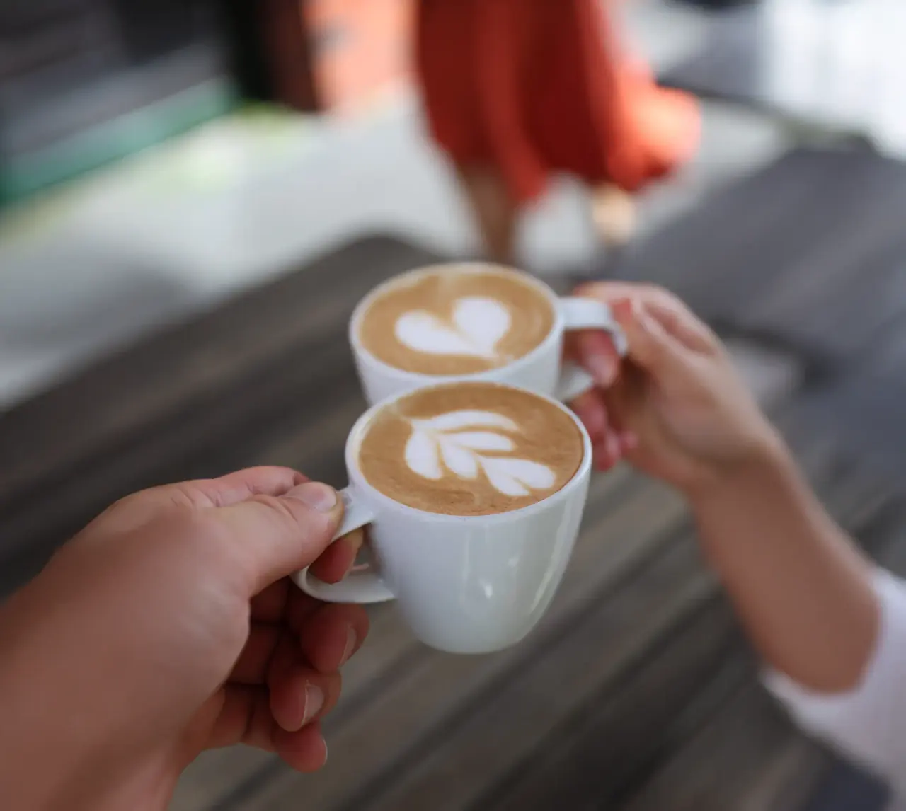 Hand hält eine Tasse Cappuccino mit Herz-Latte-Art über Holzdielen